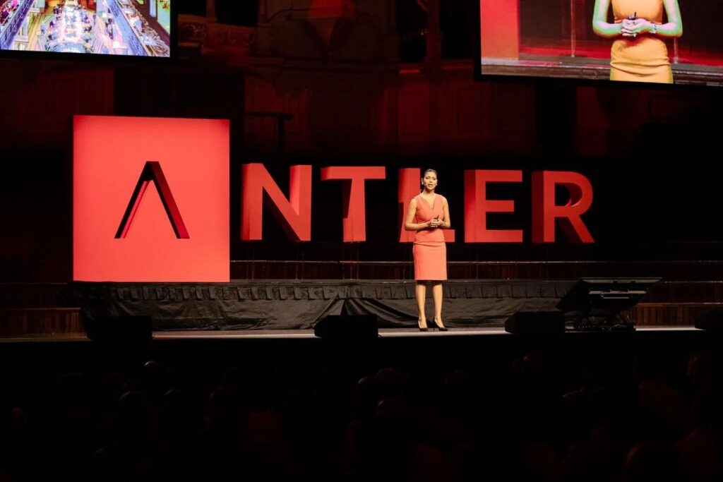 A vibrant scene from an Antler Accelerator demo day, where founders are pitching their startups to a room full of investors and mentors, with presentation slides in the background.