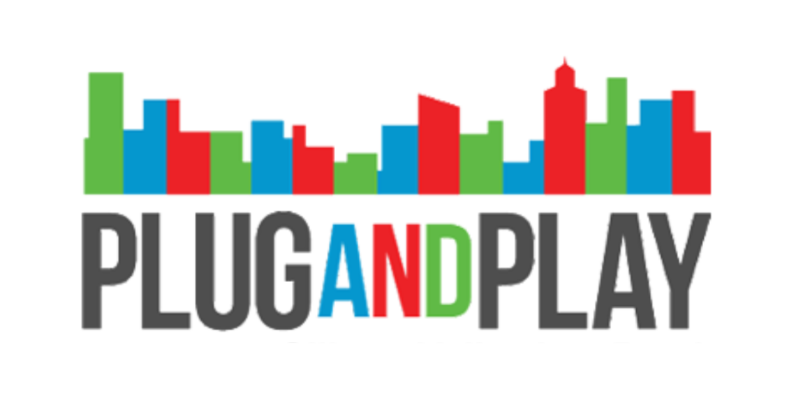 Founders networking at Plug and Play Tech Center with banners showcasing corporate innovation and startup logos.