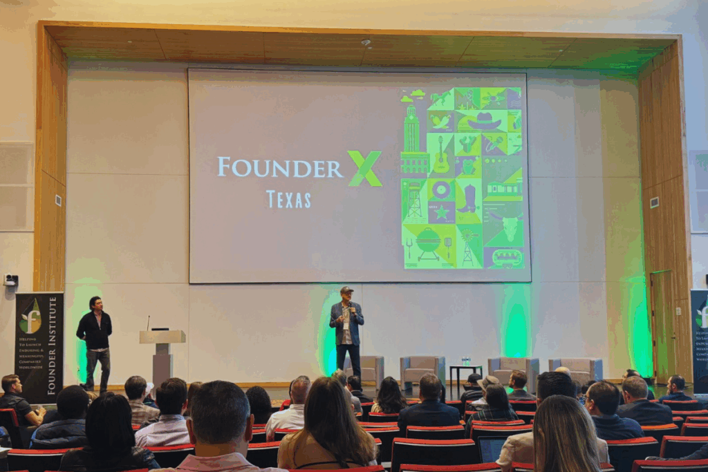 Photo of a live Founder Institute accelerator event with founders pitching on stage to mentors and an audience.