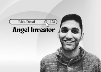 Rick Desai speaking on a Chicago tech stage, smiling with city skyline backdrop.