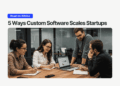 Team of startup founders collaborating around a laptop in a modern glass-walled office, discussing charts on the screen under the headline “5 Ways Custom Software Scales Startups.”