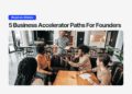 Smiling founder stands in front of a group in a modern café-style workspace, leading a discussion, with headline text above that reads “5 Business Accelerator Paths For Founders” and a blue “Read on XRaise” button.