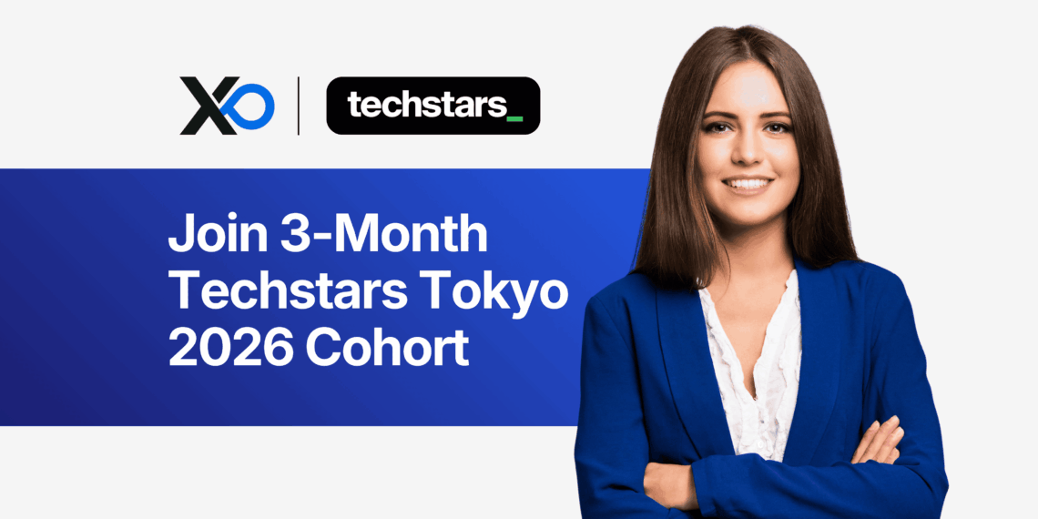 Smiling young woman in a blue blazer standing beside a banner that invites founders to join the 3-month Techstars Tokyo 2026 cohort.