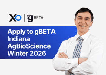 Smiling man in a white shirt and striped tie stands with folded arms beside a banner inviting founders to apply to the gBETA Indiana AgBioScience Winter 2026 accelerator.