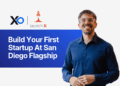 Apply to San Diego Flagship accelerator program with a smiling founder standing beside the “Build Your First Startup at San Diego Flagship” banner